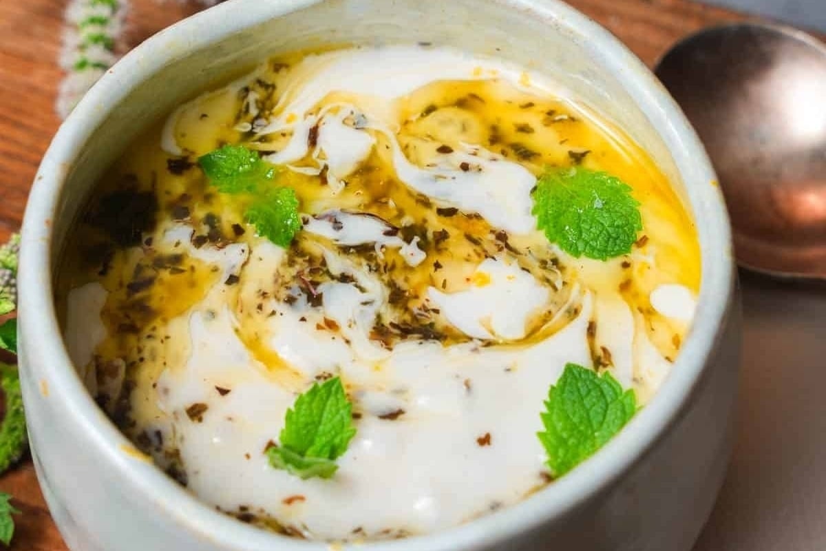 A bowl of creamy yogurt with mint leaves and a spoon.