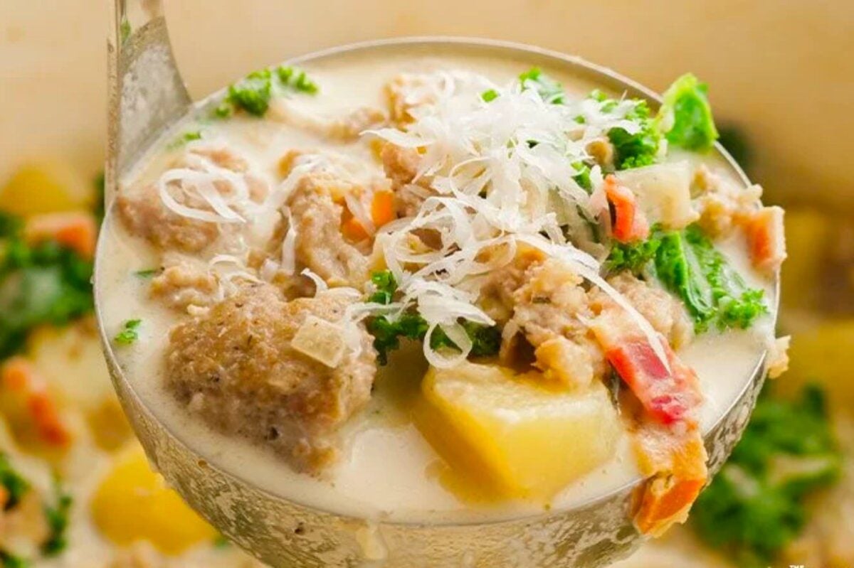 Creamy soup filled with meat and vegetables, served with a spoon.
