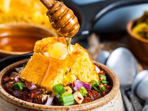 A bowl of chili with honey being poured over chili.