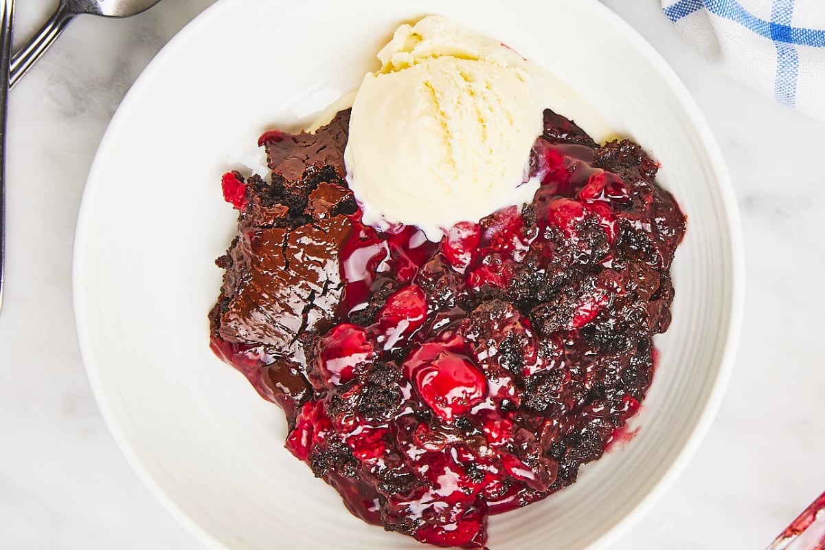 A bowl of dump cakes with ice cream and cherries.