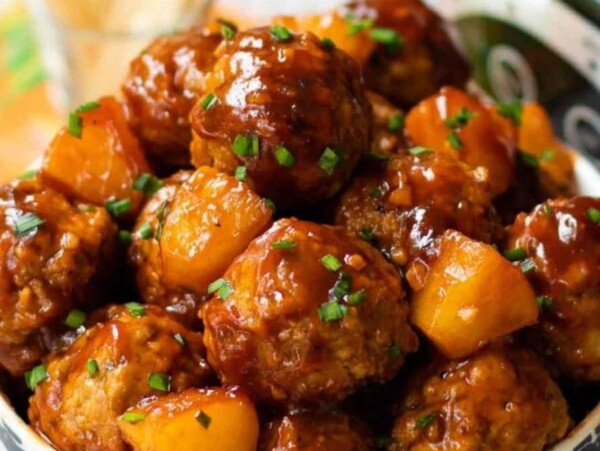 A bowl of glazed meatballs with pineapple chunks, garnished with chopped chives—perfect for your next Shared Roundup or as a tasty Slow Cooker crowd-pleaser.