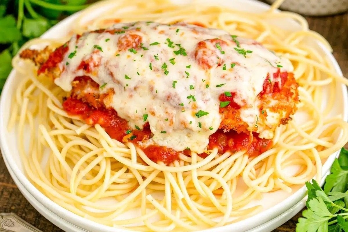 A plate of spaghetti topped with a breaded chicken parmesan covered in marinara sauce and melted mozzarella, garnished with chopped parsley, epitomizes comfort food recipes.