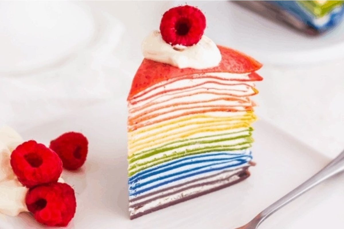Indulge in a colorful slice of rainbow crepe cake adorned with juicy raspberries.