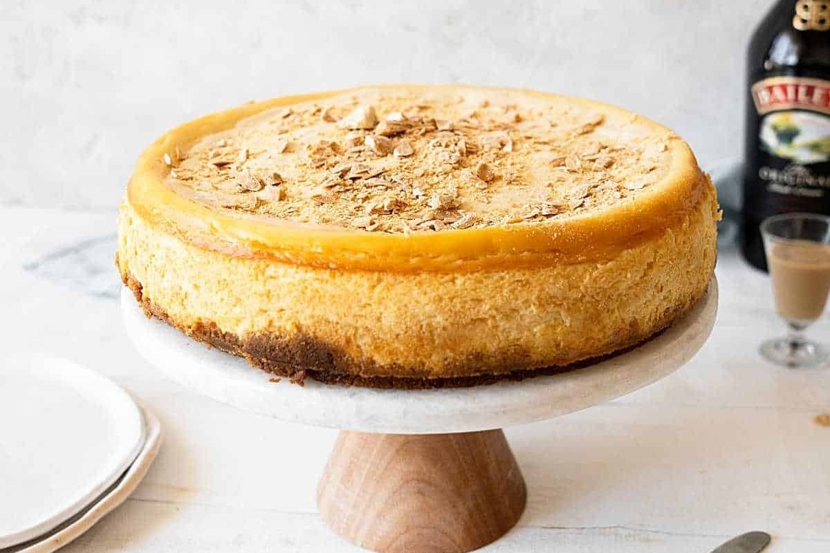 A cheesecake on a wooden stand with a bottle of bourbon, perfectly complementing St. Patrick's sweets.