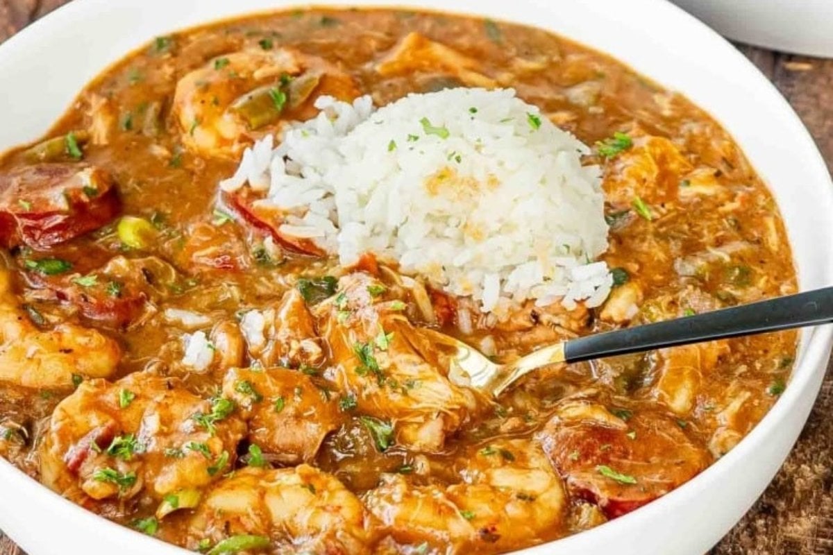 A bowl of gumbo with shrimp, sausage, vegetables, and a scoop of white rice, served with a spoon and ideal for comfort food recipes.