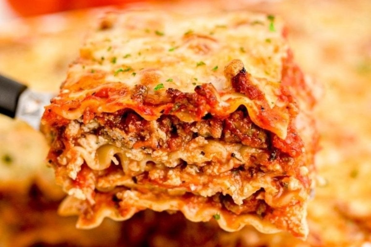 A close-up view of a slice of lasagna with layers of noodles, meat sauce, and melted cheese, garnished with chopped parsley from comfort food recipes.