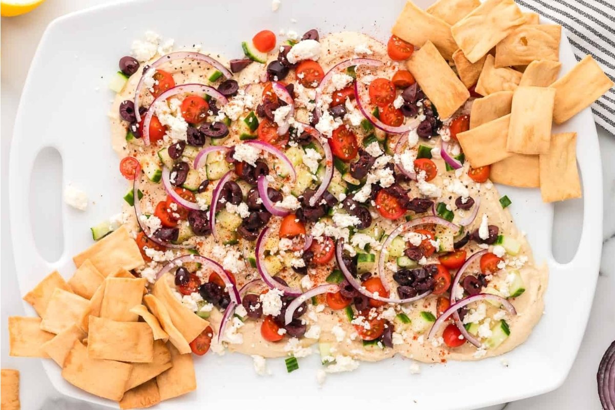 A plate of hummus with tomatoes, olives, and pita chips for girl's dinner.