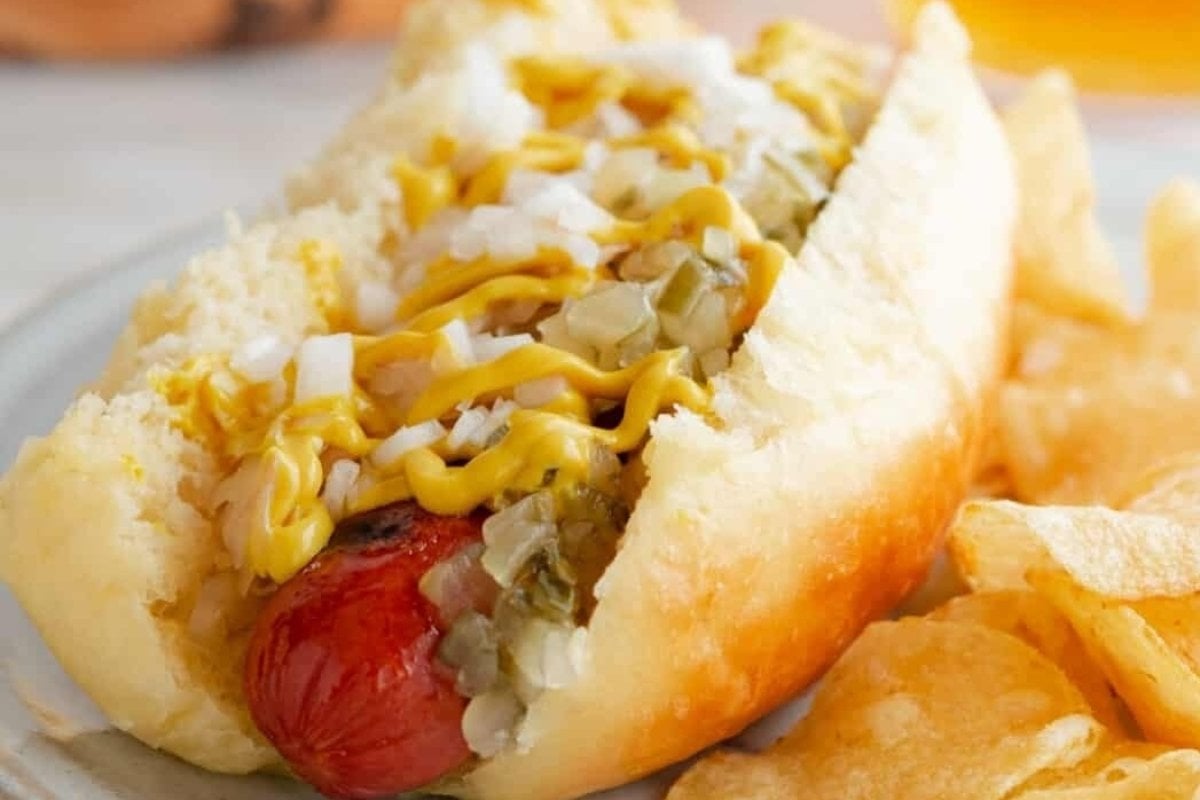 A hot dog with mustard and chips on a plate featuring bread recipes.