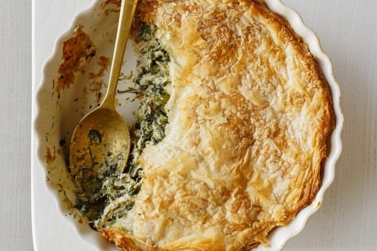 A spinach and cheese pie, perfect for comfort food recipes, in a white dish with a golden crust, partially served with a spoon.