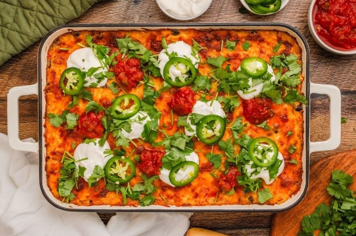 Mexican lasagna in a baking dish with jalapenos and sour cream, inspired by taco flavored recipes.