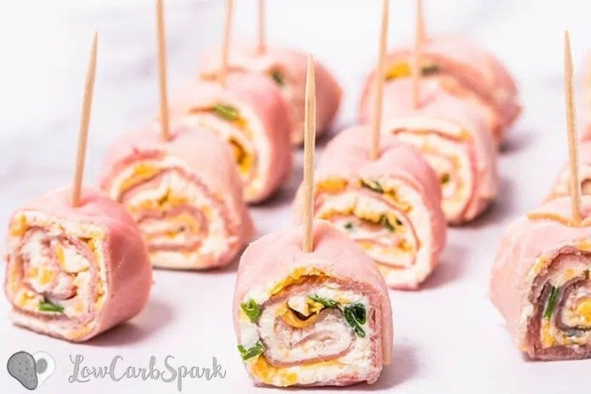 Ham and cheese bites for dinner, each secured with a toothpick, garnished with green herbs on a light background.