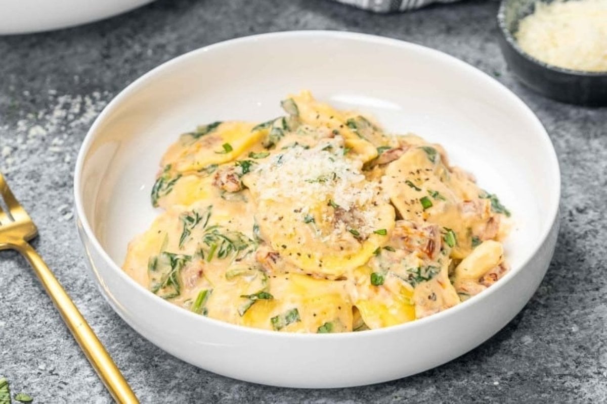 A bowl of creamy ravioli topped with herbs and grated cheese, with a gold fork on the side, perfect for comfort food recipes.