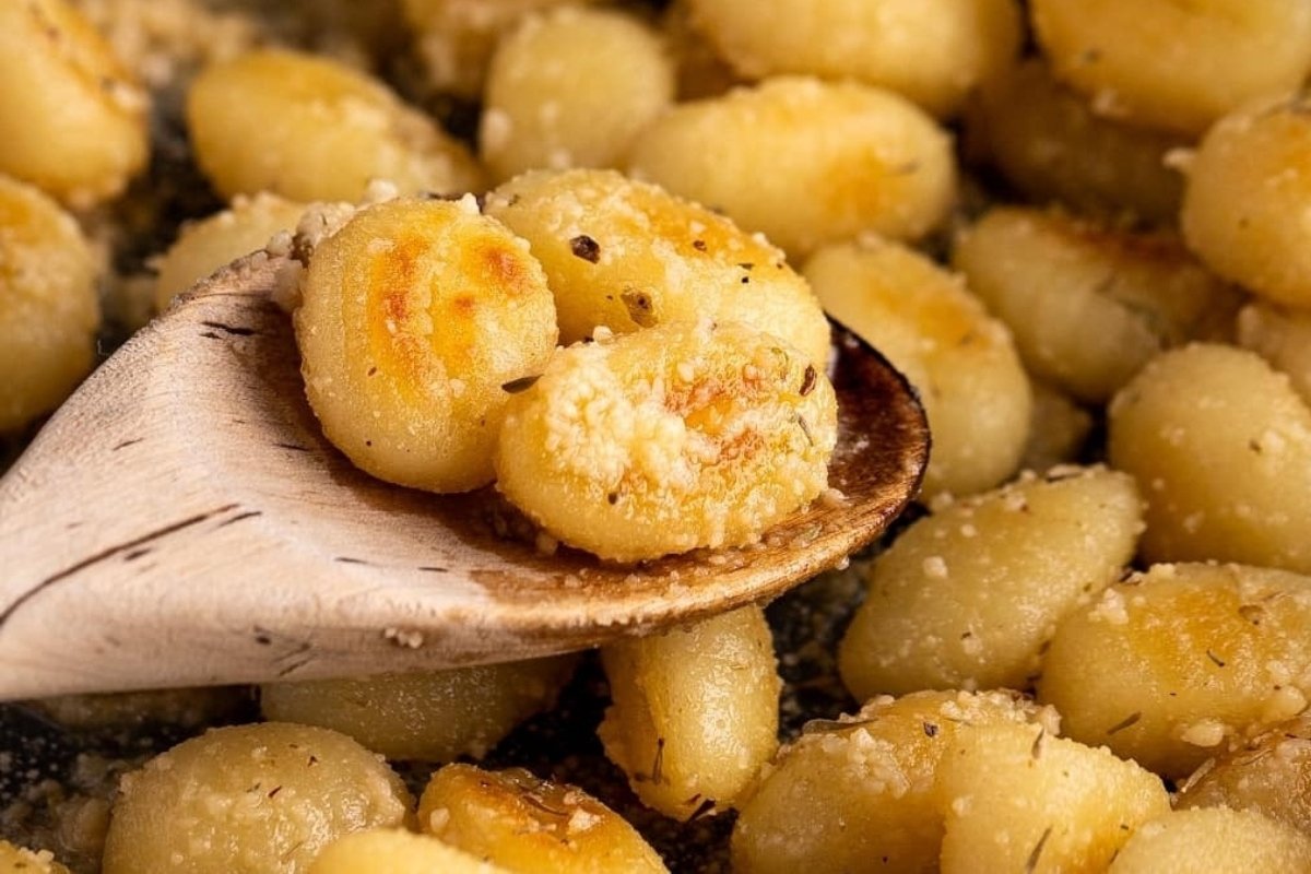 Close-up of golden-brown gnocchi on a wooden spoon, sprinkled with grated cheese and herbs—a perfect comfort food delight.