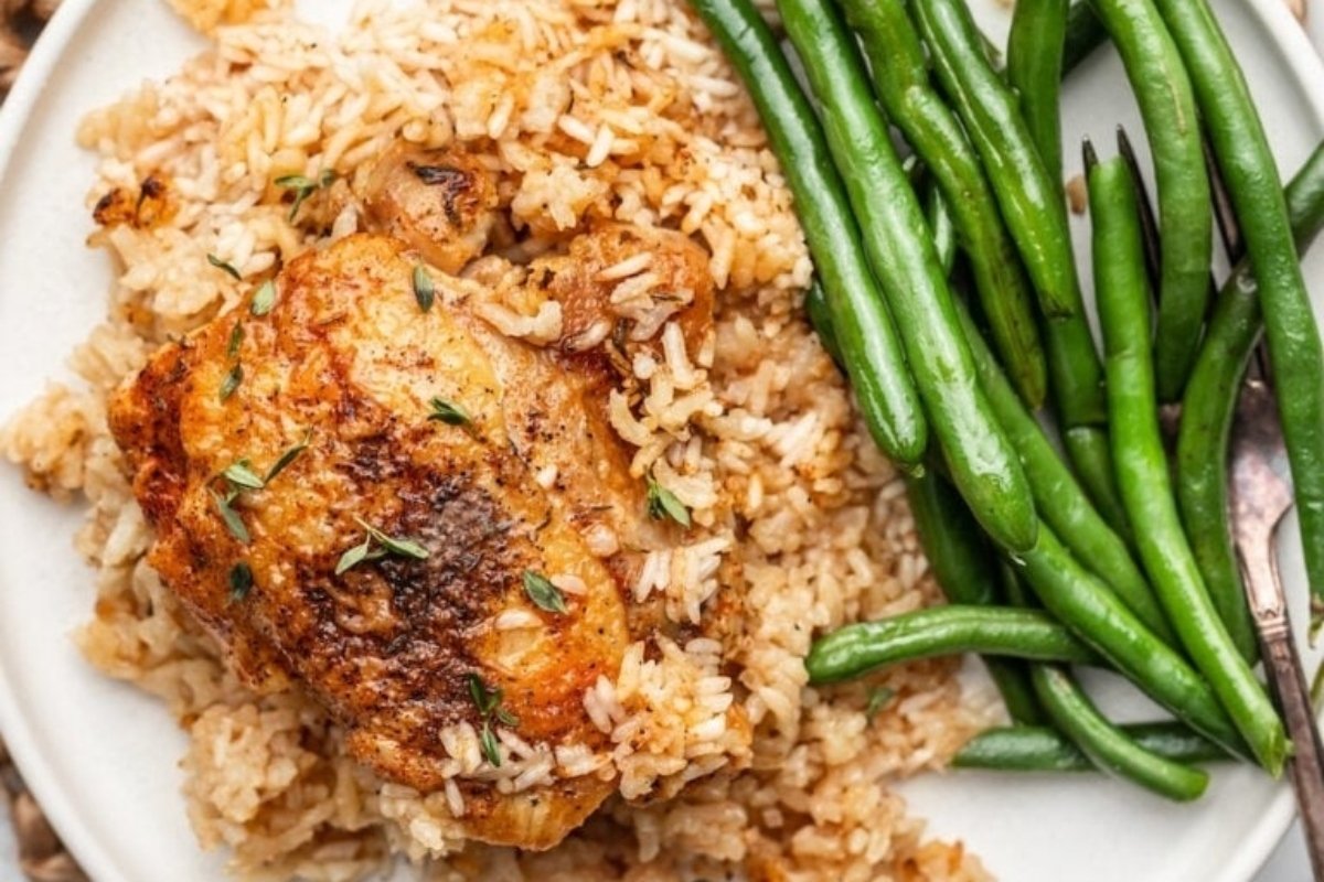 A plate of comfort food featuring baked chicken over seasoned rice, served with fresh green beans on the side.
