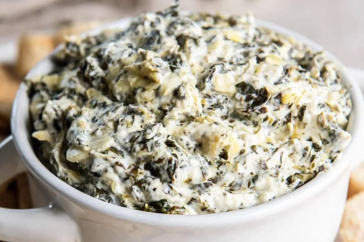 Creamy spinach and artichoke dip served in a white bowl, with a chunky, textured appearance—perfect for your collection of slow cooker game day recipes.