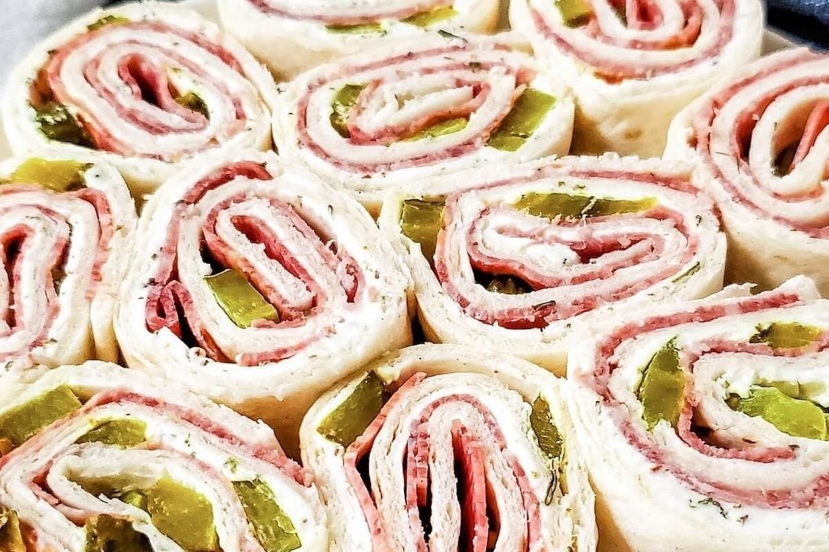 Close-up of tortilla roll-ups filled with cream cheese, deli meat, and pickles arranged on a plate, perfect as bites for dinner.