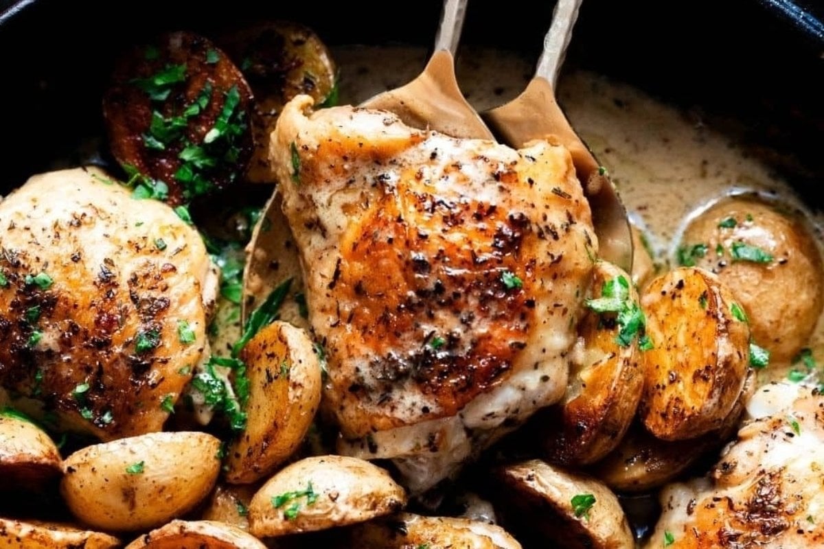 Roasted chicken thighs with a crispy skin, garnished with chopped parsley, served with golden brown potatoes in a skillet - a classic comfort food recipe.