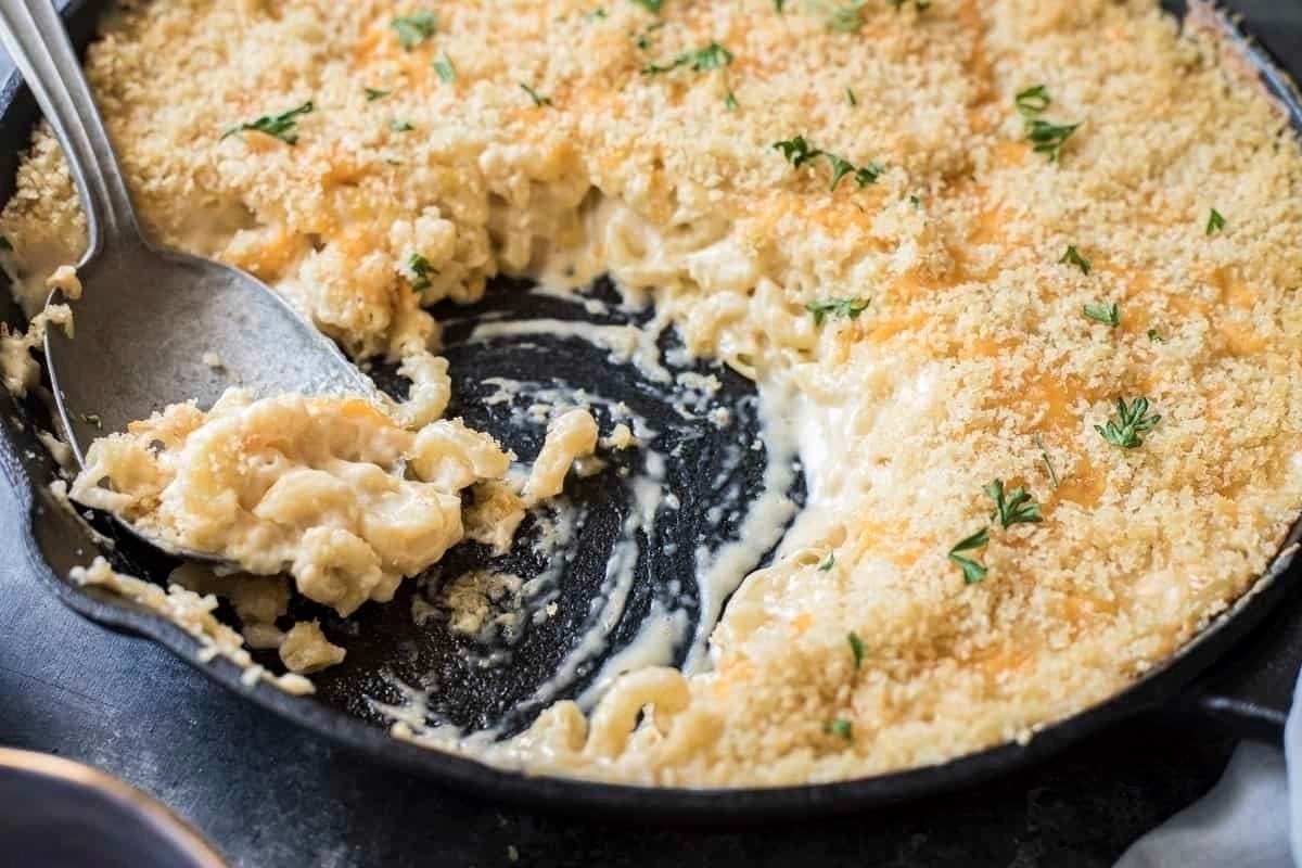 A black skillet containing creamy macaroni and cheese, half eaten, topped with golden breadcrumbs and garnished with parsley - a classic example of comfort food recipes.
