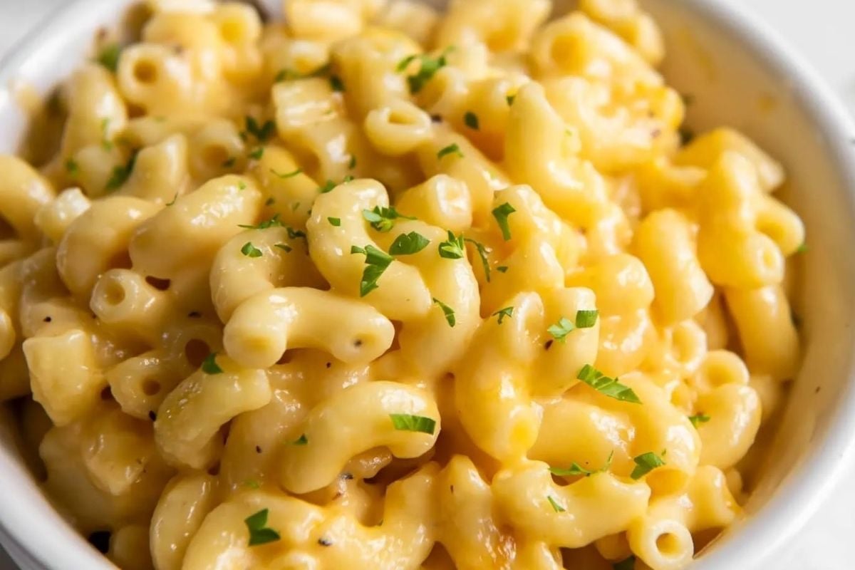 Creamy macaroni and cheese, a perfect addition to your slow cooker game day recipes, topped with chopped fresh parsley in a white bowl.