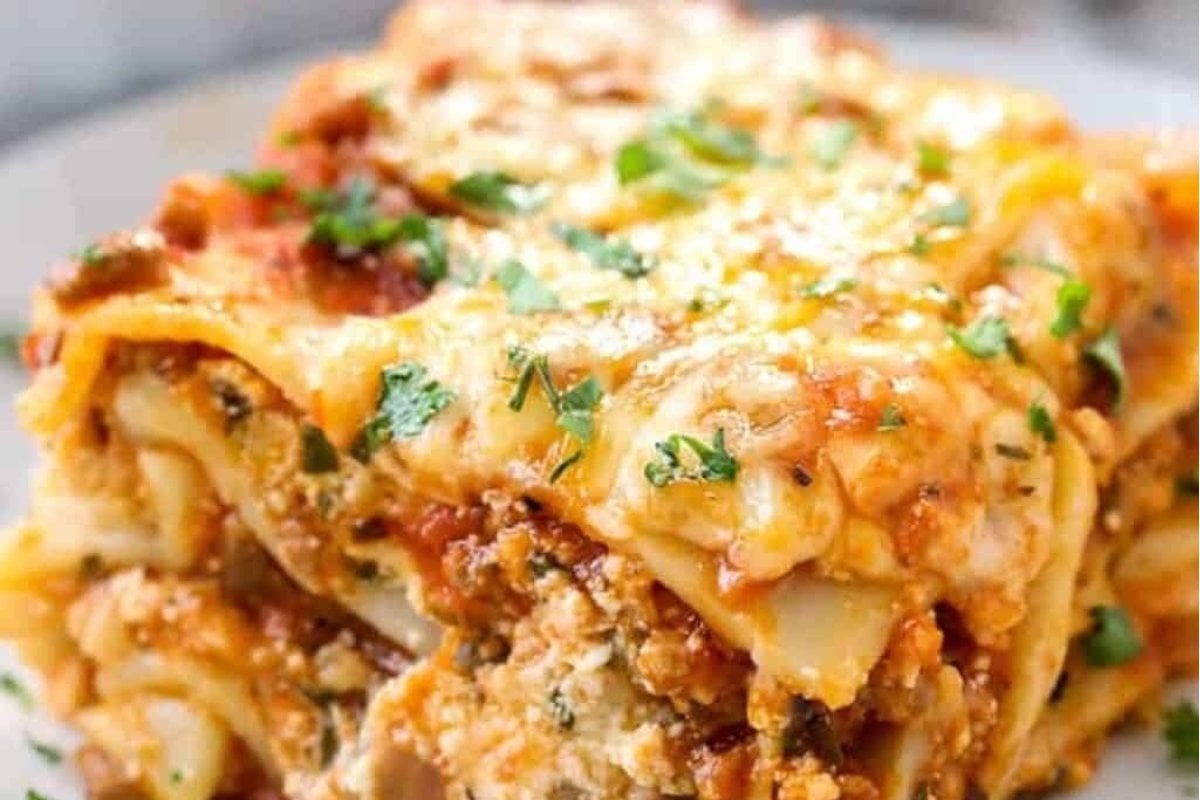 A close-up image of a slice of lasagna with melted cheese, garnished with parsley on a white plate, showcasing comfort food recipes.