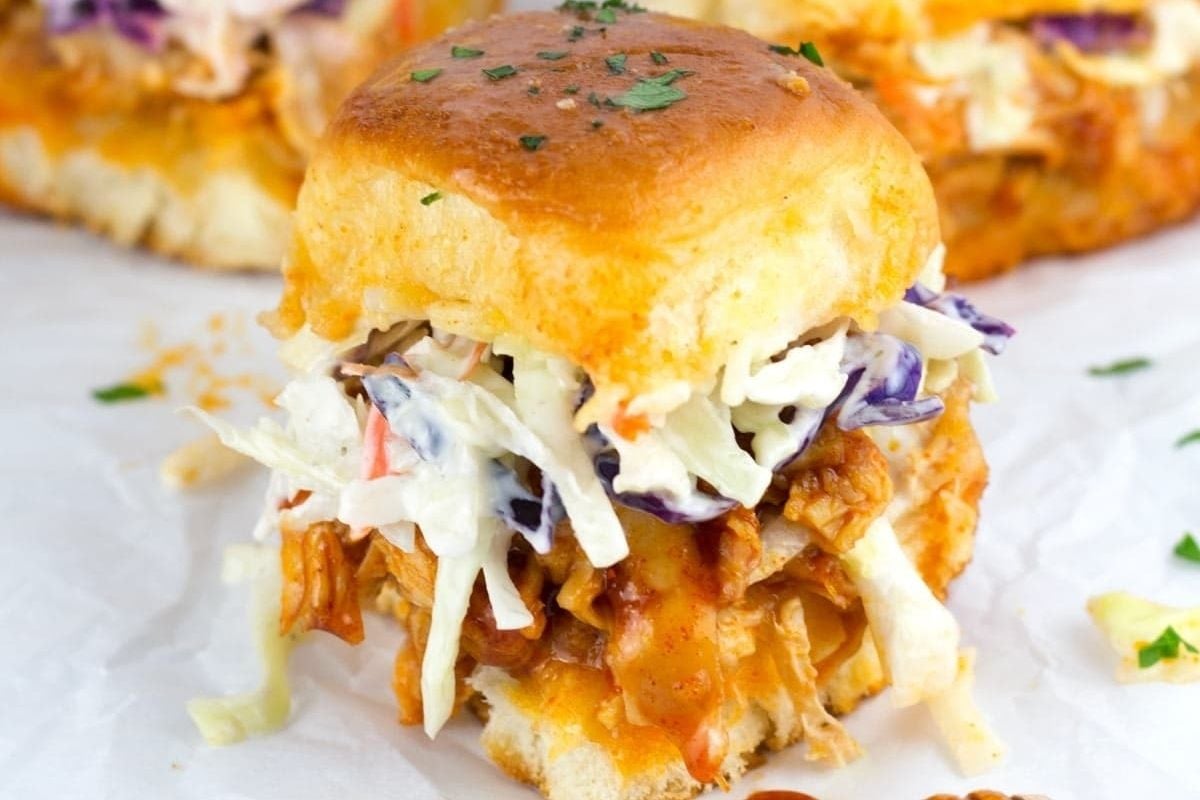 A perfect game day bite size treat—Buffalo chicken slider topped with creamy coleslaw on a soft bun, garnished with chopped parsley.