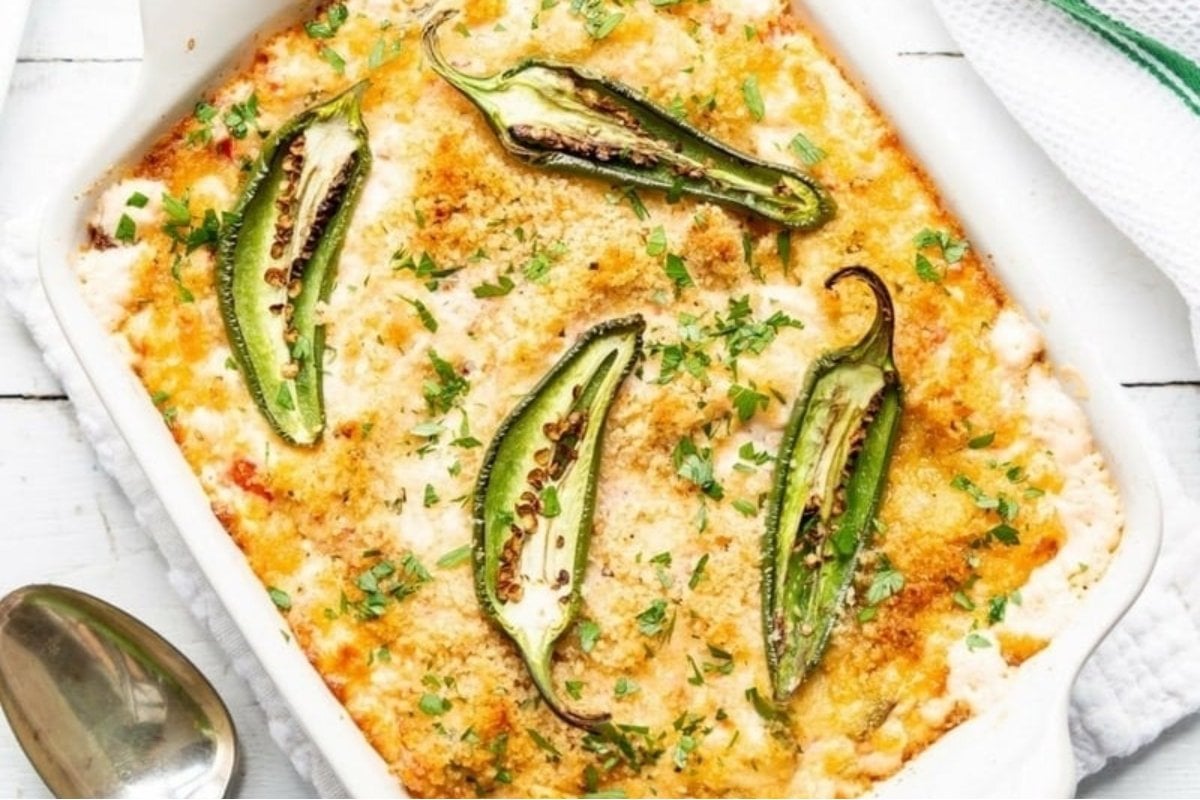 A baked casserole topped with melted cheese, breadcrumbs, and sliced jalapeños, garnished with fresh parsley in a white dish, perfect as bites for dinner.