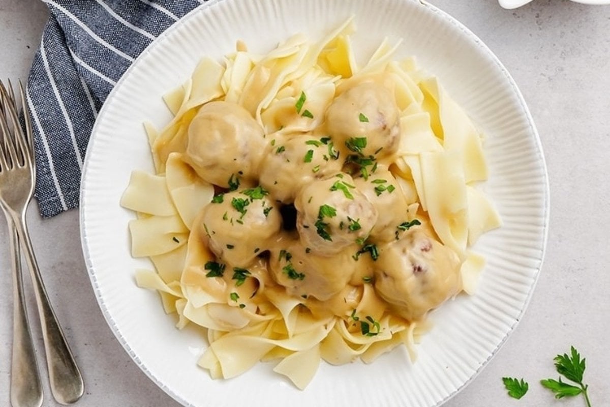 A plate of Swedish meatballs served over wide egg noodles, garnished with chopped parsley, viewed from above&mdash;perfect for comfort food recipes.