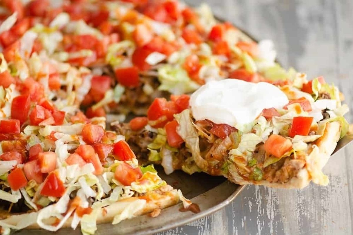 Mexican taco-flavored pizza on a plate with toppings and sour cream.