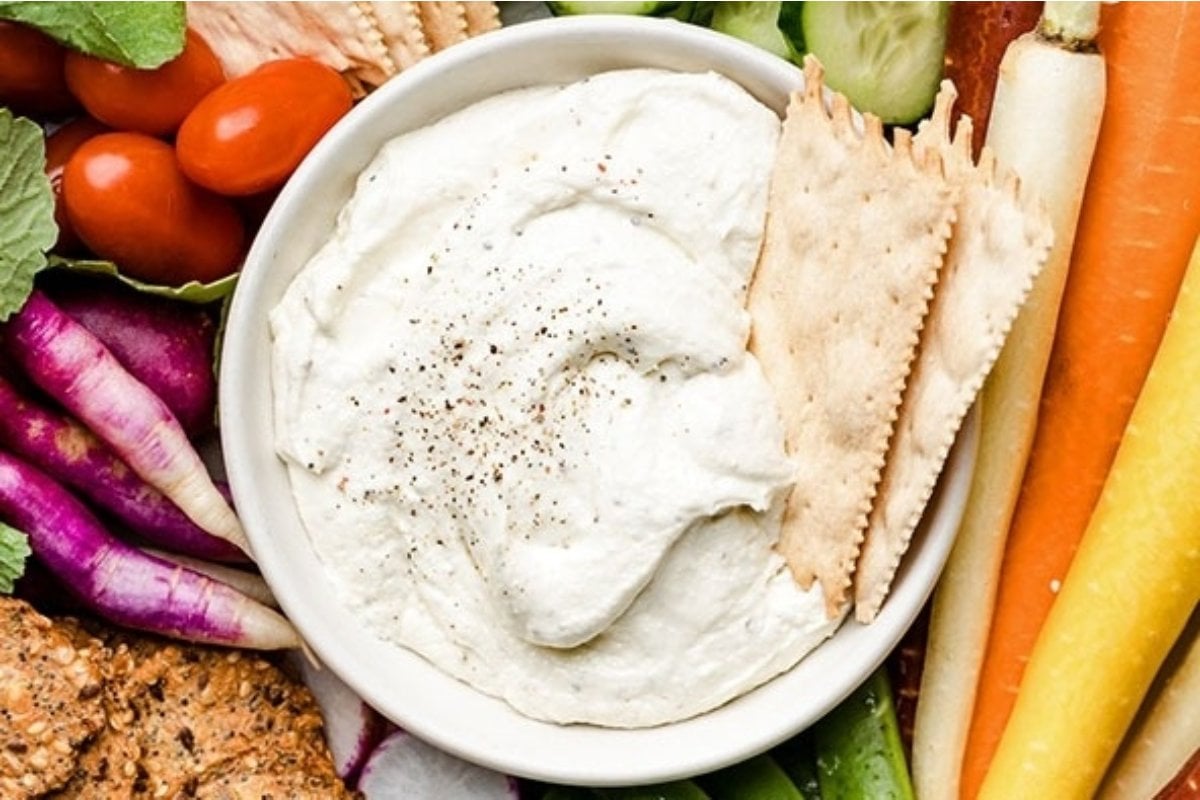 A bowl of creamy hummus surrounded by fresh vegetables and pita bread slices, perfect as bites for dinner.