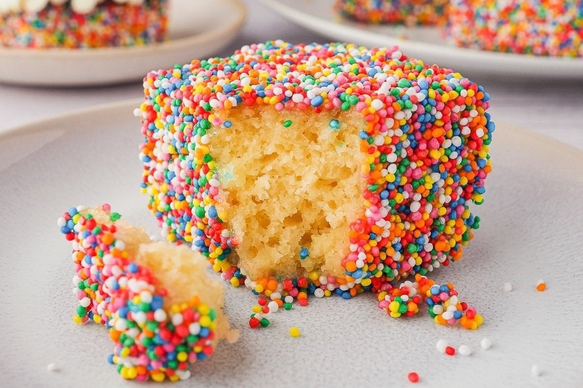 Colorful rainbow cupcakes with sprinkles are displayed on a plate.