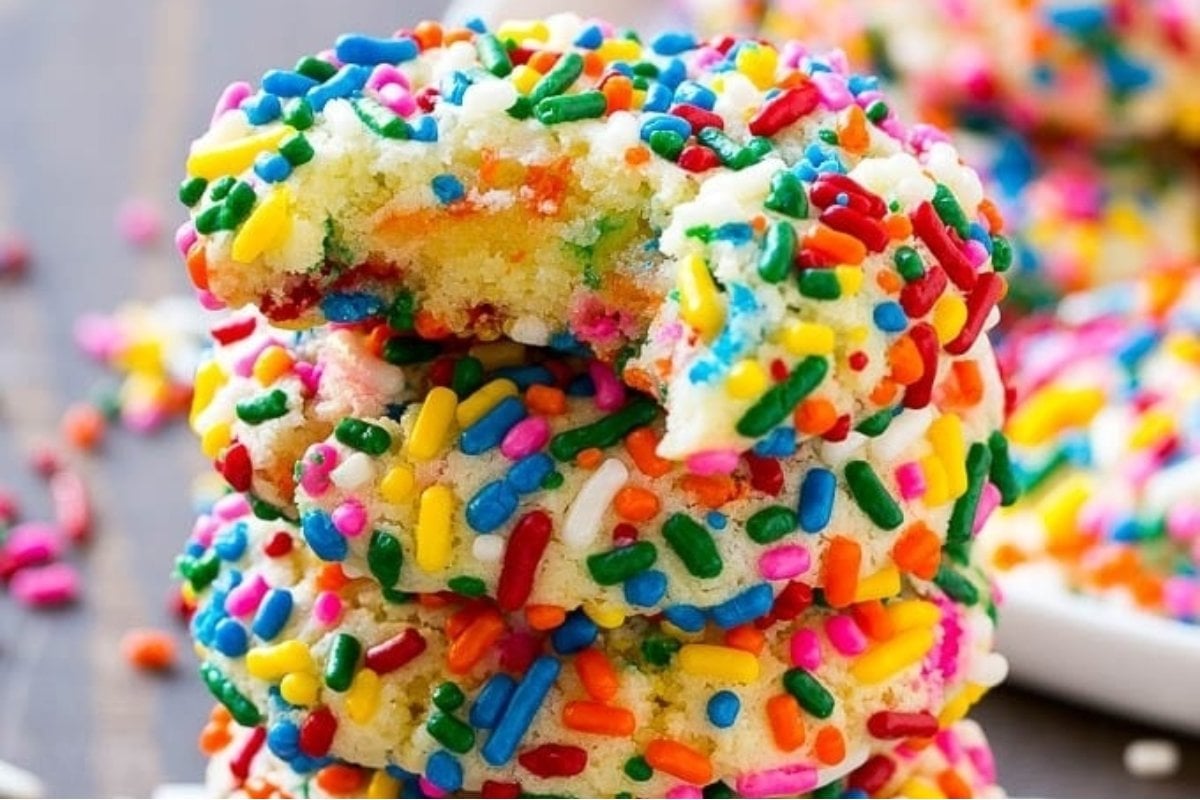 A stack of rainbow sprinkle cookies with a bite taken out.