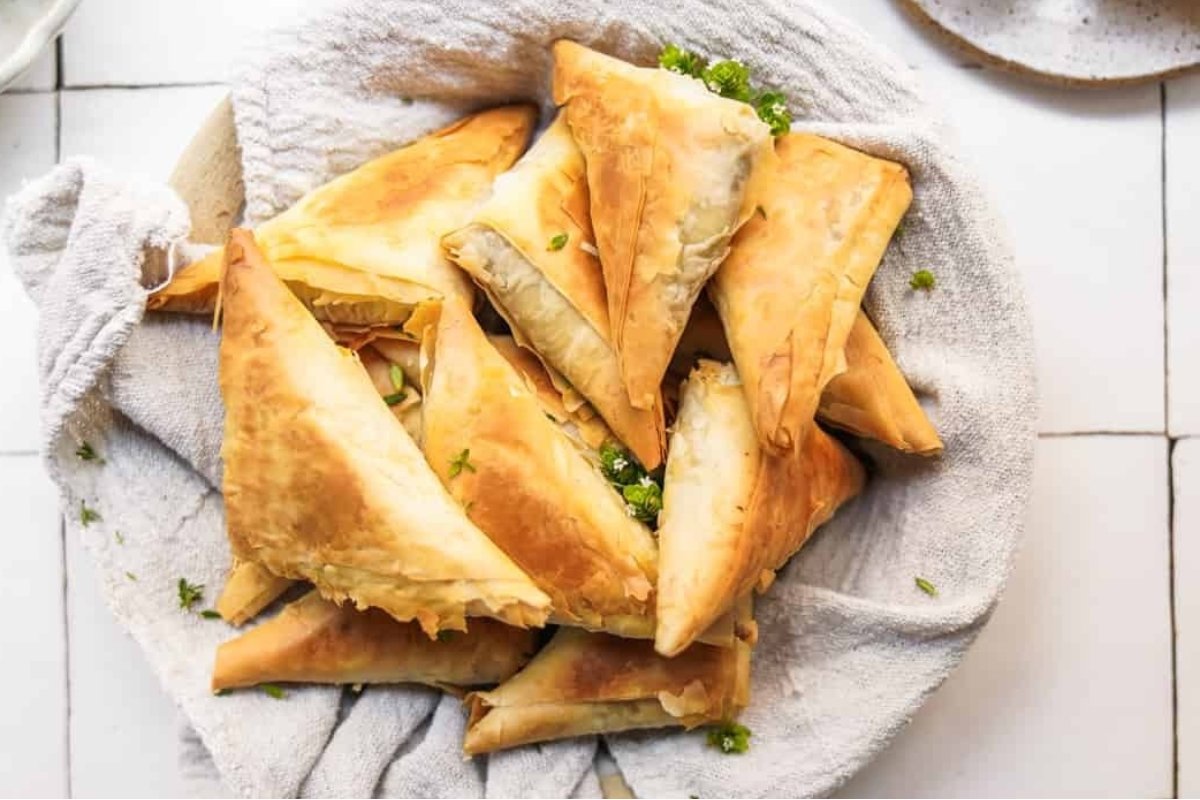 Golden, flaky samosas arranged on a towel-lined plate, garnished with a sprinkle of fresh herbs—a perfect comfort food treat.