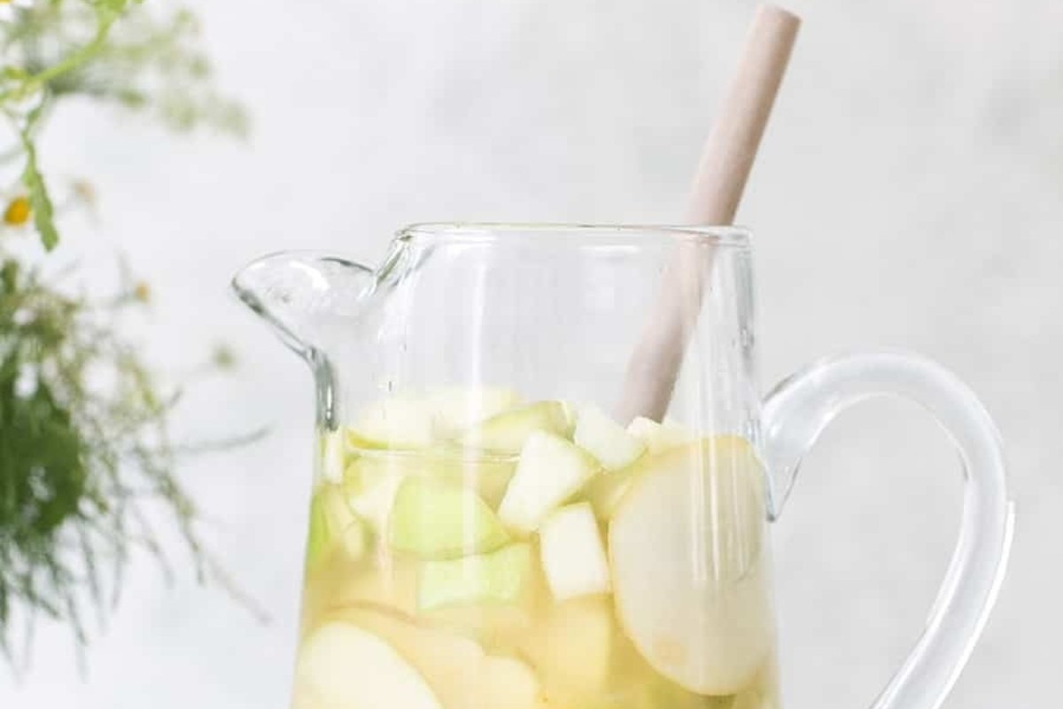 A pitcher of apple sangria, perfect for St Patrick's drinks, with sliced apples and a wooden spoon.
