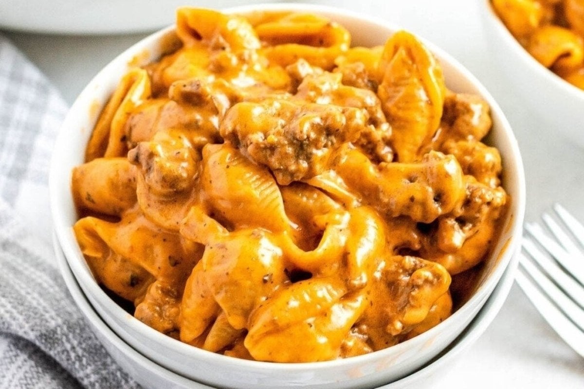 A bowl of creamy tomato pasta with ground meat, served on a white tablecloth, perfect as a comfort food recipe.