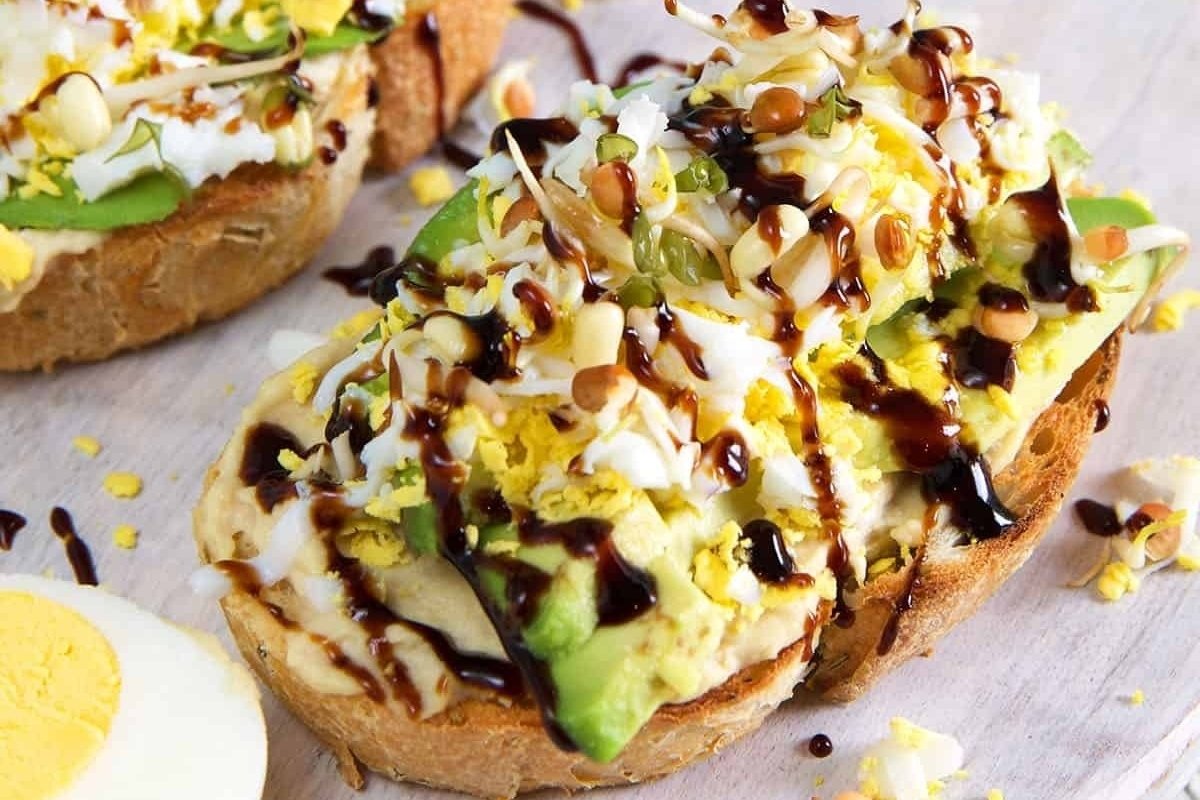 A girl prepares a sandwich with avocado, egg, and bacon on a cutting board for dinner.
