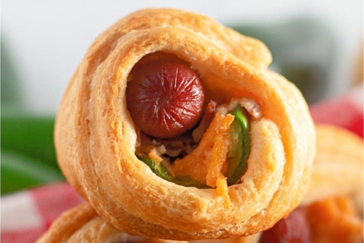 Close-up of a sausage roll with a visible cross-section showing a sausage, cheese, and green pepper wrapped in a golden-brown crust, perfect as bites for dinner.