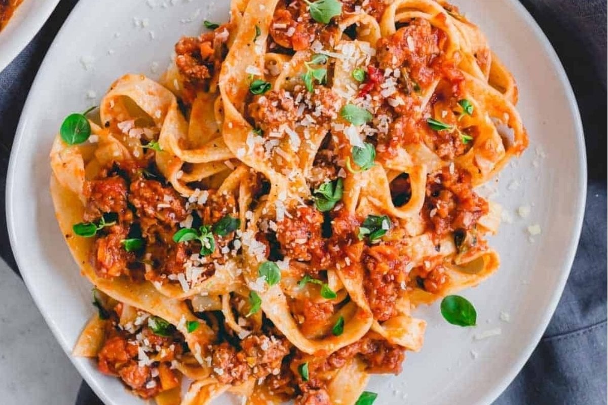 A plate of tagliatelle pasta topped with meat sauce, grated cheese, and fresh herbs—true comfort food at its finest.
