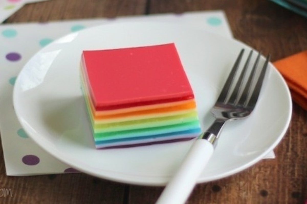 A plate with a fork and a stack of rainbow colored food, perfect for trying out some new rainbow recipes!