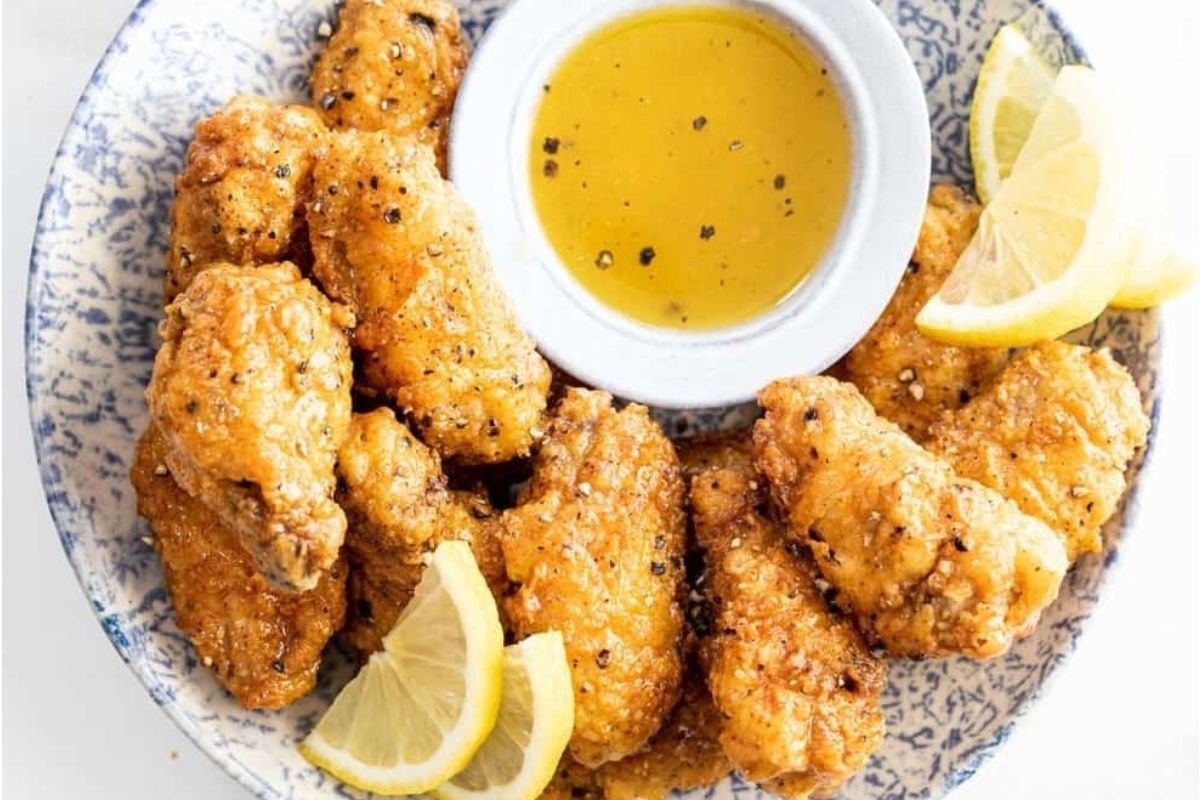 Enjoy bite size fried chicken wings on a plate with lemon wedges and a bowl of honey mustard dipping sauce—perfect for a game day treat.