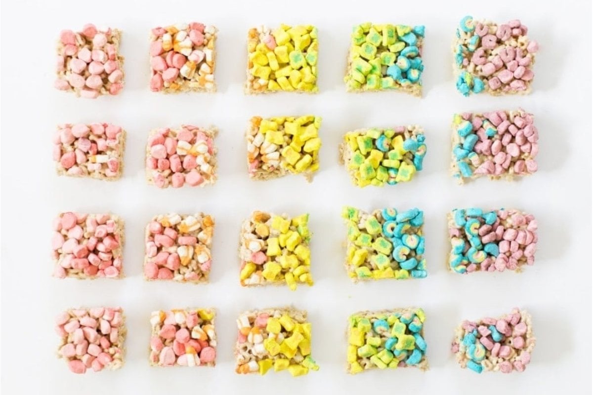 Colorful rainbow rice krispie treats are arranged on a white surface.