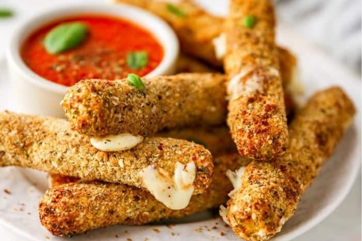 Bite-size mozzarella sticks with melted cheese, served on a plate with a small bowl of marinara sauce for dipping—perfect for game day snacking.