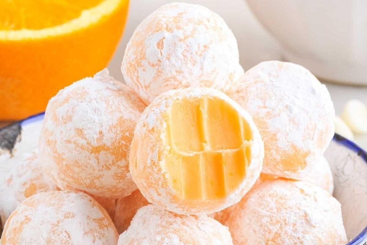 A bowl full of citrus-flavored orange balls coated in powdered sugar.