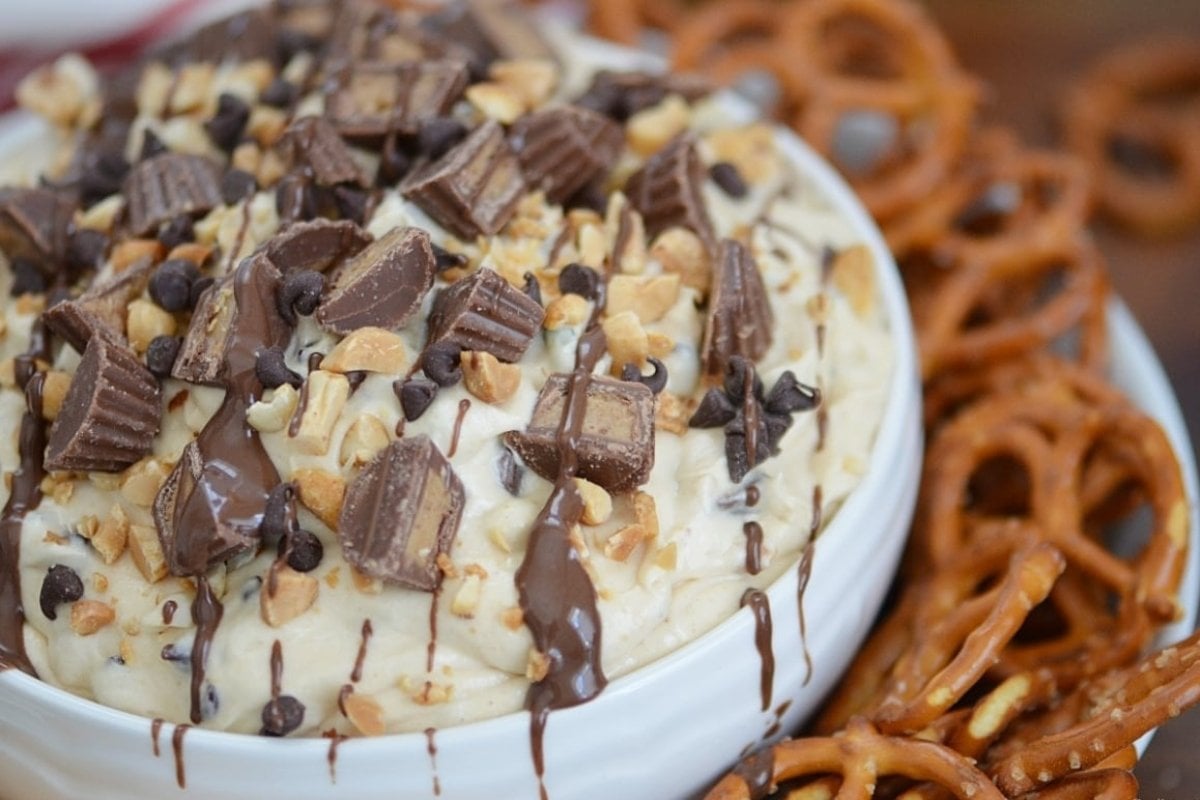 Close-up of a dessert bowl with creamy ice cream topped with chopped chocolate bars, nuts, chocolate chips, pretzels, and drizzled with chocolate syrup, perfect for bites after dinner.