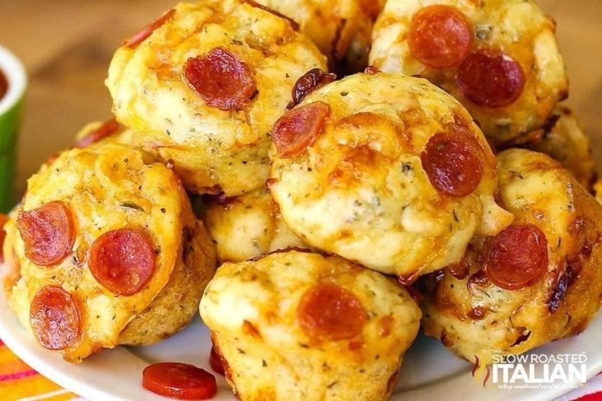 Mini pepperoni pizza muffins stacked on a plate, topped with melted cheese and pepperoni slices—perfect bites for dinner.