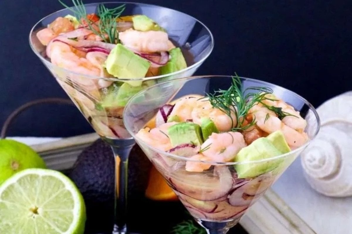 Two shrimp cocktails in martini glasses, garnished with dill, accompanied by slices of lime and a whole avocado, perfect as bites for dinner.