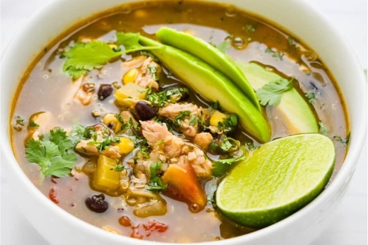 A bowl of taco flavored Mexican chicken soup with avocado and lime.