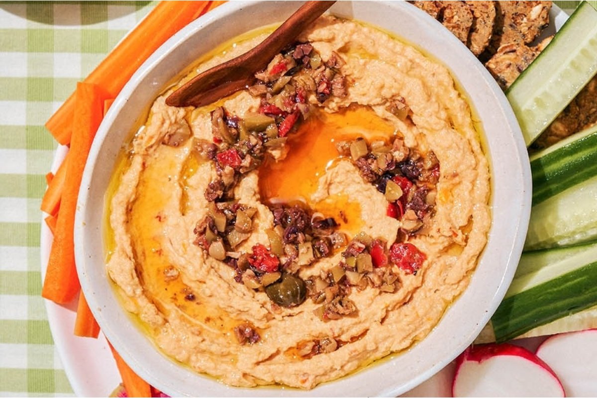 A girl's dinner featuring a bowl of hummus with carrots and celery.