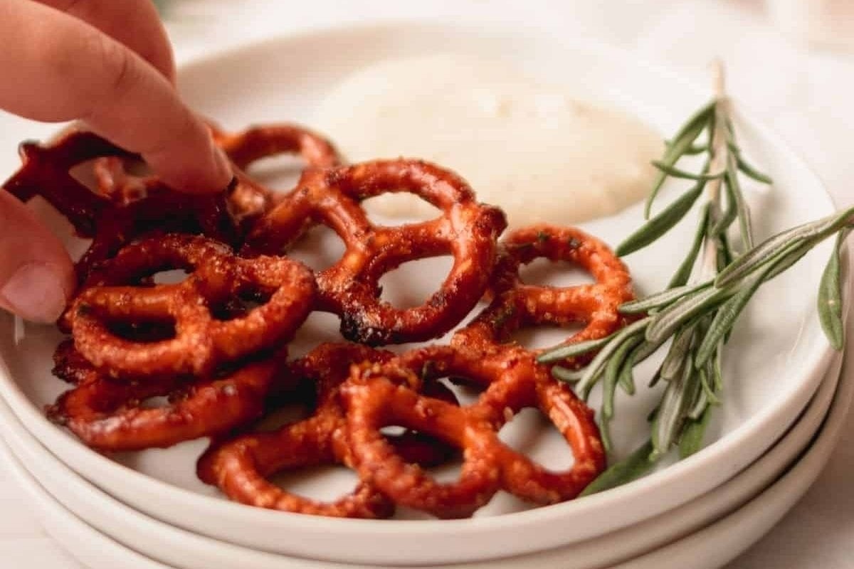 A close-up image of a person's hand picking up fried calamari bites for dinner from a white plate, served with a side of white dipping sauce and garnished with rosemary.