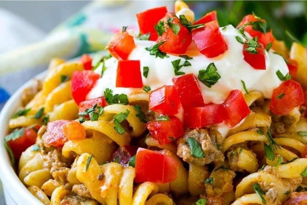 A bowl of taco flavored pasta with meat, tomatoes, and sour cream.