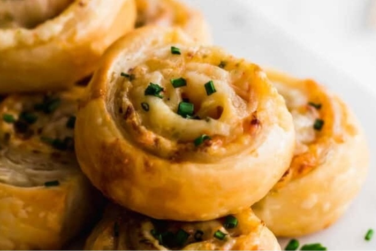 Close-up of cheese and chive pinwheels on a plate, freshly baked with golden-brown crust and garnished with chopped chives, perfect as bites for dinner.